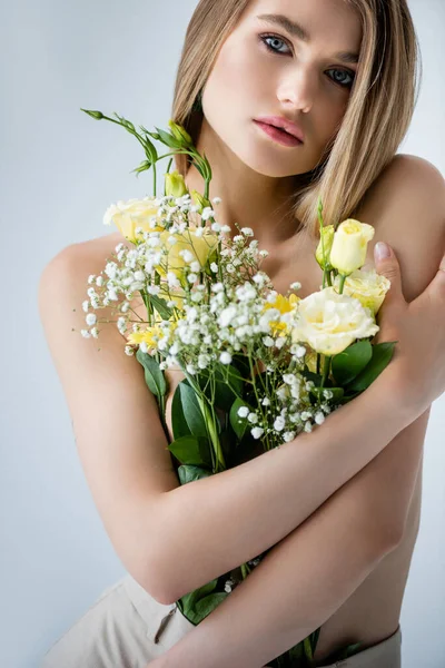 Junges Model mit nackten Schultern umarmt Blumen auf grau — Stockfoto