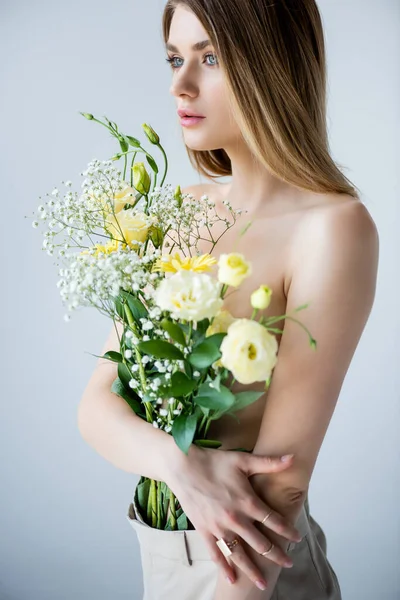 Молода жінка з квітами в штанях стоїть на сірому — стокове фото