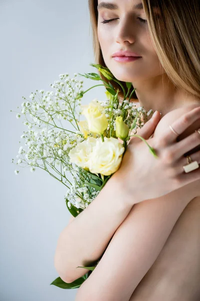 Junges Model mit geschlossenen Augen umarmt Blumen auf grau — Stockfoto