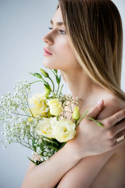 Woman with naked shoulders embracing flowers on grey — Stock Photo