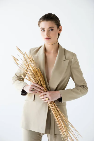Молода жінка в бежевому формальному одязі тримає пшеницю на білому — стокове фото