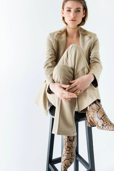 Young model in suit poising while sitting on stool on white background — Stock Photo