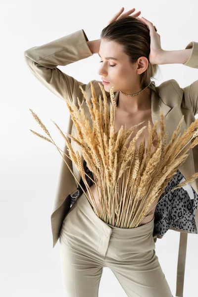 Modelo elegante en ropa formal beige con espiguillas de trigo posando aisladas en blanco - foto de stock