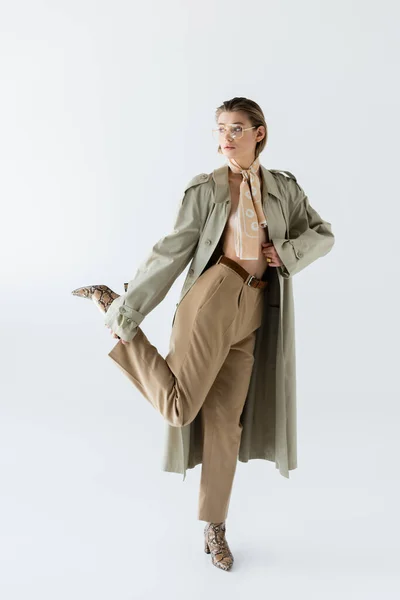 Pleine longueur de femme à la mode dans des lunettes, trench coat et écharpe posant sur blanc — Photo de stock