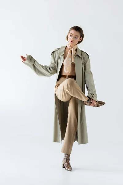 Full length of young woman in glasses, trench coat and scarf posing on white — Stock Photo