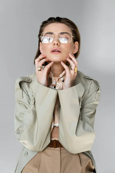 Trendige junge Frau mit Brille, Trenchcoat und Schal posiert auf grau — Stockfoto