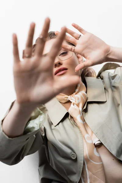 Top view of young woman in glasses, trench coat and scarf lying while gesturing on white — стоковое фото