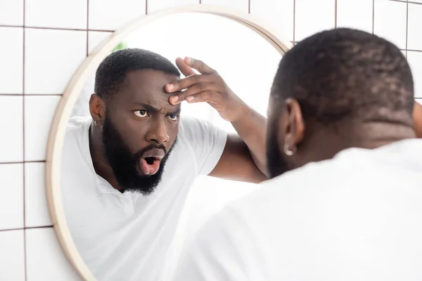 Шокований афроамериканський чоловік дивиться на зморшки у дзеркалі — стокове фото