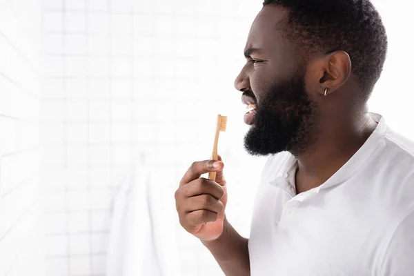 Vista lateral de un hombre afroamericano desagradable cepillándose los dientes - foto de stock