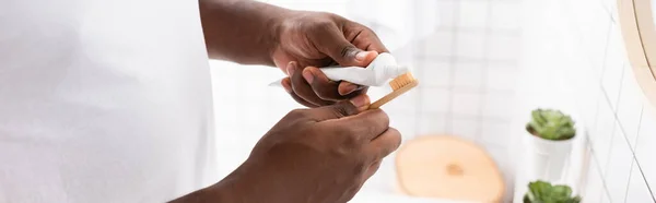 Plano panorámico del hombre afroamericano exprimiendo pasta de dientes del tubo - foto de stock