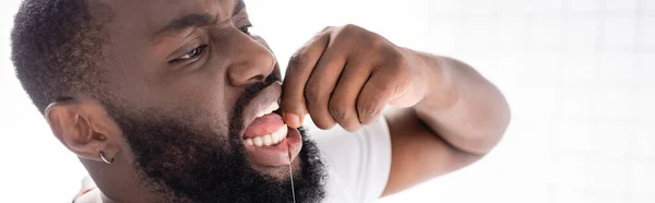 Panoramic view of afro-american man using dental floss — Stock Photo
