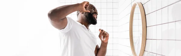 Panoramic view of afro-american using dental floss and looking in mirror — Stock Photo