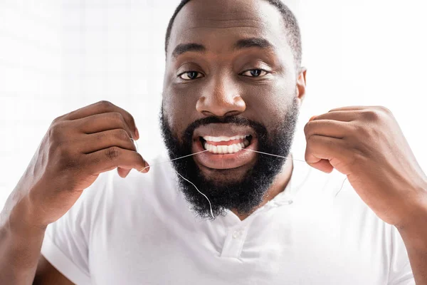 Retrato del hombre afroamericano usando hilo dental y mirando a la cámara - foto de stock