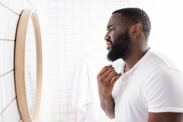 Vue latérale de l'homme afro-américain malheureux regardant la barbe dans le miroir — Photo de stock