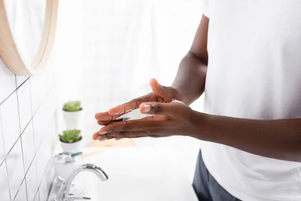 Vista recortada del hombre afroamericano aplicando espuma de afeitar con las manos - foto de stock