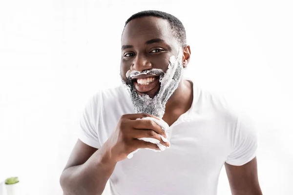 Улыбающийся афро-американец с пеной для бритья на лице, смотрящий в камеру — стоковое фото