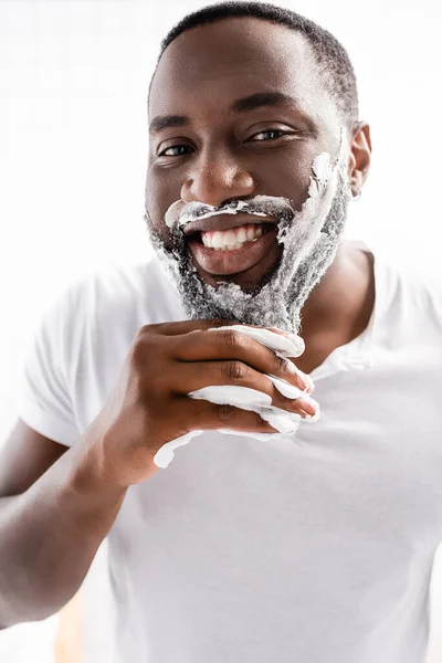 Homme afro-américain souriant avec mousse à raser sur le visage regardant la caméra — Photo de stock