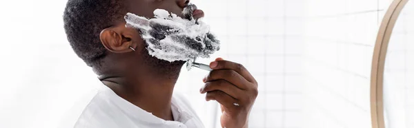 Plan panoramique de l'homme afro-américain rasant barbe avec rasoir — Photo de stock
