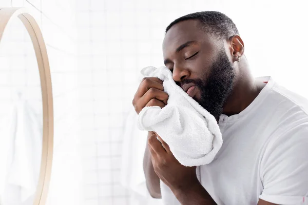 Hombre afroamericano con los ojos cerrados secando barba con toalla suave - foto de stock