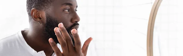 Plano panorámico del hombre afroamericano aplicando cura para fortalecer el crecimiento de la barba - foto de stock