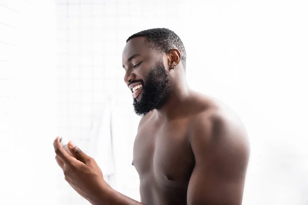 Hombre afroamericano sonriente sosteniendo desodorante en la mano - foto de stock