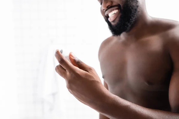 Vista recortada de hombre afroamericano sonriente sosteniendo desodorante en la mano — Stock Photo