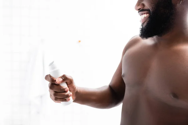 Vista recortada de hombre afroamericano sonriente sosteniendo desodorante en la mano - foto de stock