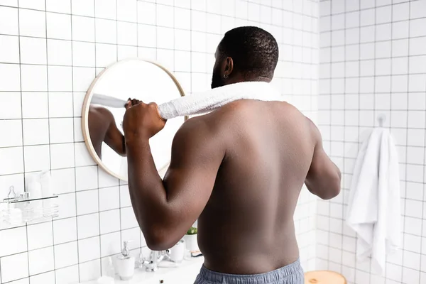 Rückansicht eines afroamerikanischen Mannes, der mit einem Handtuch im Nacken in den Spiegel blickt — Stockfoto