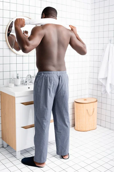 Toute la longueur de l'homme afro-américain debout dans la salle de bain avec serviette derrière le cou — Photo de stock