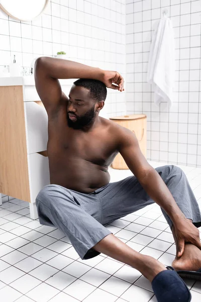 Homme afro-américain avec la main vers le haut assis sur le sol et sentant aisselle — Photo de stock