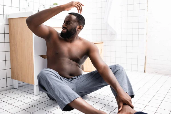 Афроамериканец с поднятой вверх рукой сидит на полу и пахнет подмышками — стоковое фото