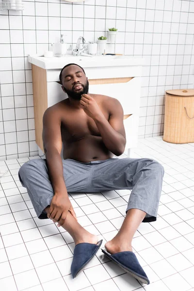 Nachdenklicher afroamerikanischer Mann sitzt auf dem Boden und berührt Bart — Stockfoto