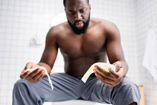 Hombre afro-americano confundido tratando tiras de cera - foto de stock