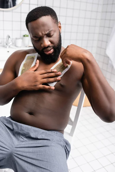 Afro-americano homem aplicando tiras de cera no peito — Fotografia de Stock