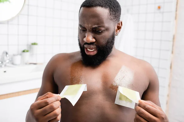 Shocked afro-american man tearing off wax strips — Stock Photo