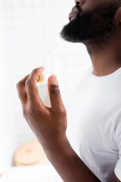 Cropped view of afro-american man in white t-shirt using perfume — Stock Photo