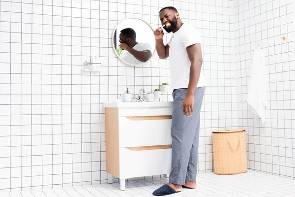 Longueur totale de l'homme afro-américain brossant les dents et regardant en arrière — Photo de stock