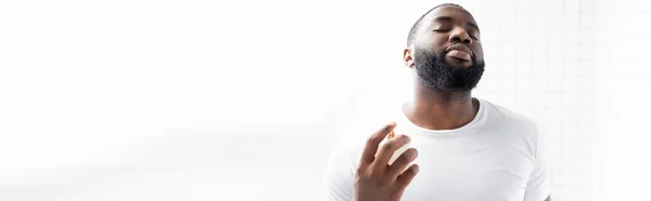 Plano panorámico del hombre afroamericano en camiseta blanca usando perfume — Stock Photo