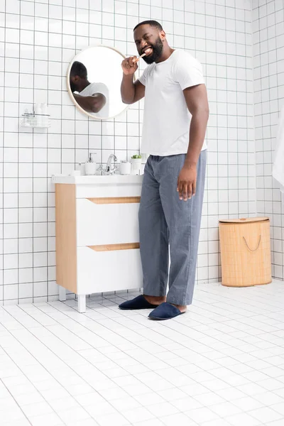 Longitud completa de hombre afroamericano cepillarse los dientes en el baño - foto de stock