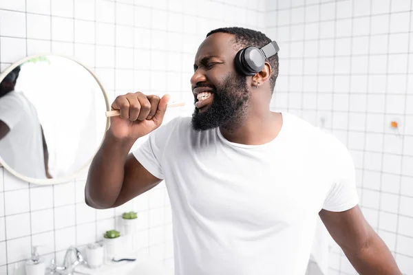 Afro-american man with headphones singing in toothbrush — Stock Photo