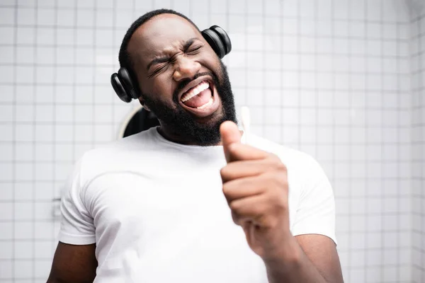 Афроамериканський чоловік з навушниками, що співають у зубній щітці — стокове фото