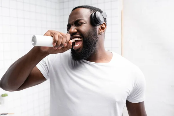 Homme afro-américain avec écouteurs chantant dans la brosse à dents — Photo de stock