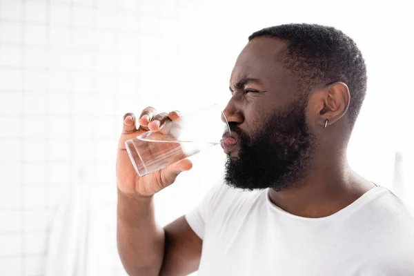 Hombre afroamericano haciendo muecas y bebiendo agua - foto de stock