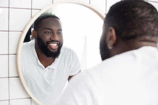 Hombre afroamericano sonriente mirándose en el espejo - foto de stock