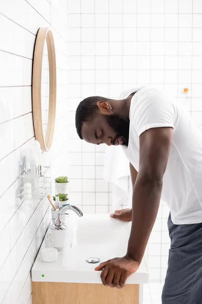 Müder afroamerikanischer Mann mit geschlossenen Augen lehnt sich an Waschbecken — Stockfoto