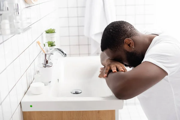 Hombre afro-americano cansado apoyado cabeza en el fregadero - foto de stock