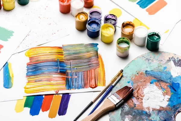 Gouache paints, paintbrushes and abstract colorful brushstrokes on paper on white background — Stock Photo