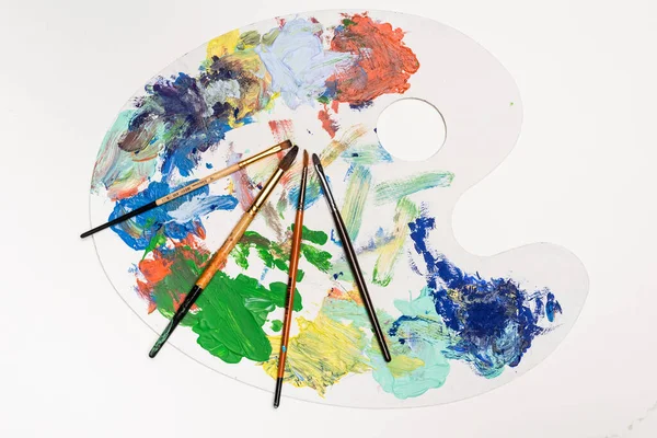 Top view of palette with paints and paintbrushes isolated on white — Stock Photo