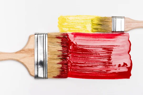 Top view of paintbrushes near colorful red and yellow paint brushstrokes on white background — Stock Photo