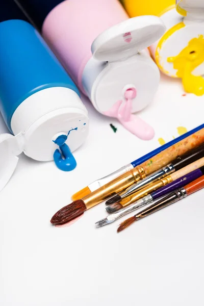 Squeezed acrylic paints near paintbrushes on white background — Stock Photo